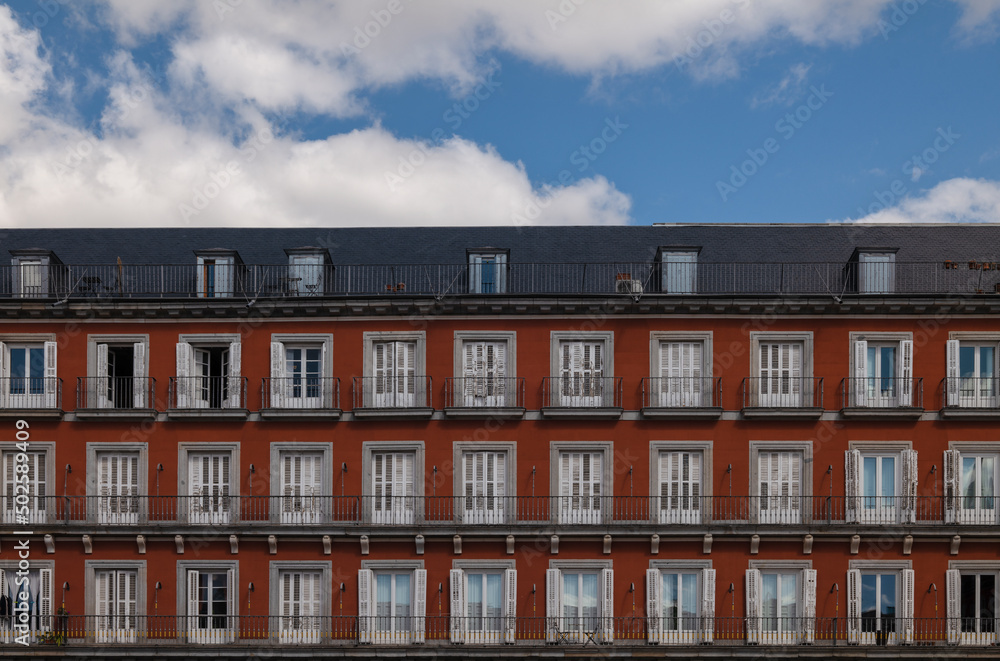 Facade of red building with balconies against cloudy sky. Madrid, Spain