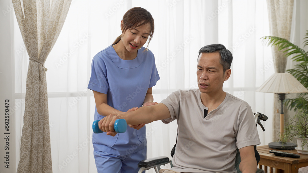 Fototapeta premium asian female nursing aide helping mature male wheelchair user to do rehab exercise with dumbbells in the living room. home health care and senior fitness concept