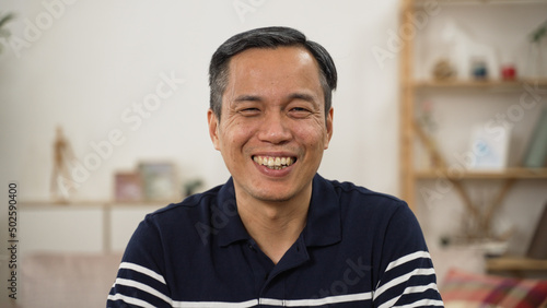 shoulder shot portrait of a cheerful Chinese elderly male in casual wear smiling at the camera in a modern bright home interior