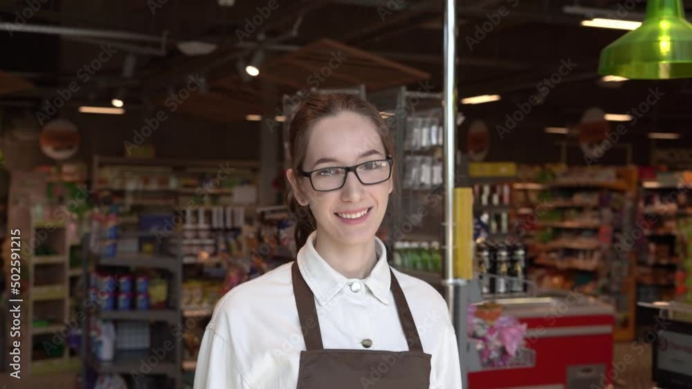 The girl supermarket cashier smiles for the camera. High quality FullHD footage The girl supermarket cashier smiles for the camera. High quality FullHD footage