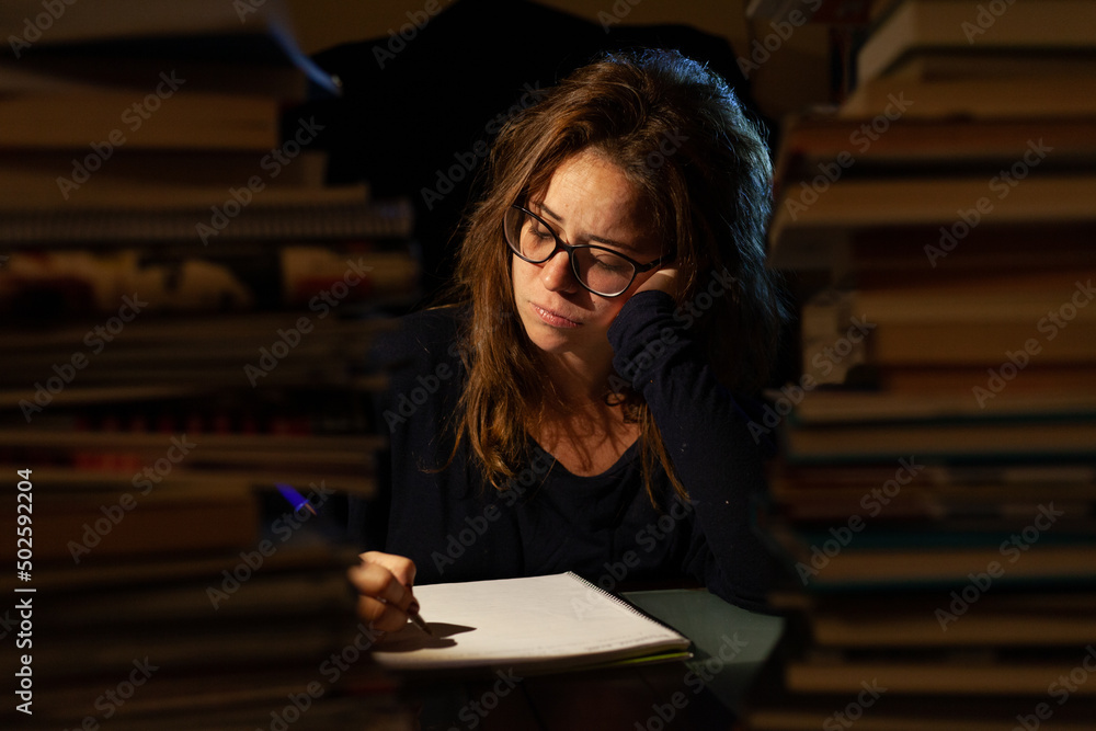 An overburdened woman studying in a library for final exams