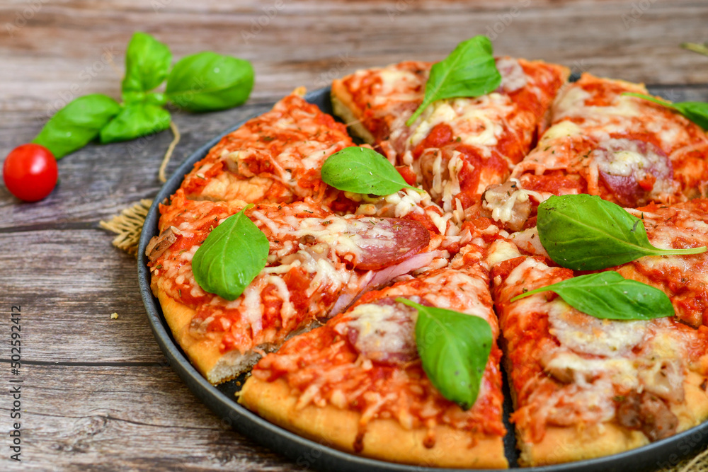  Close up of   classic  Italian Pizza   with Ham and salami . Fresh basil,tomato sauce ,mozzarella cheese , mushrooms and  green peppers