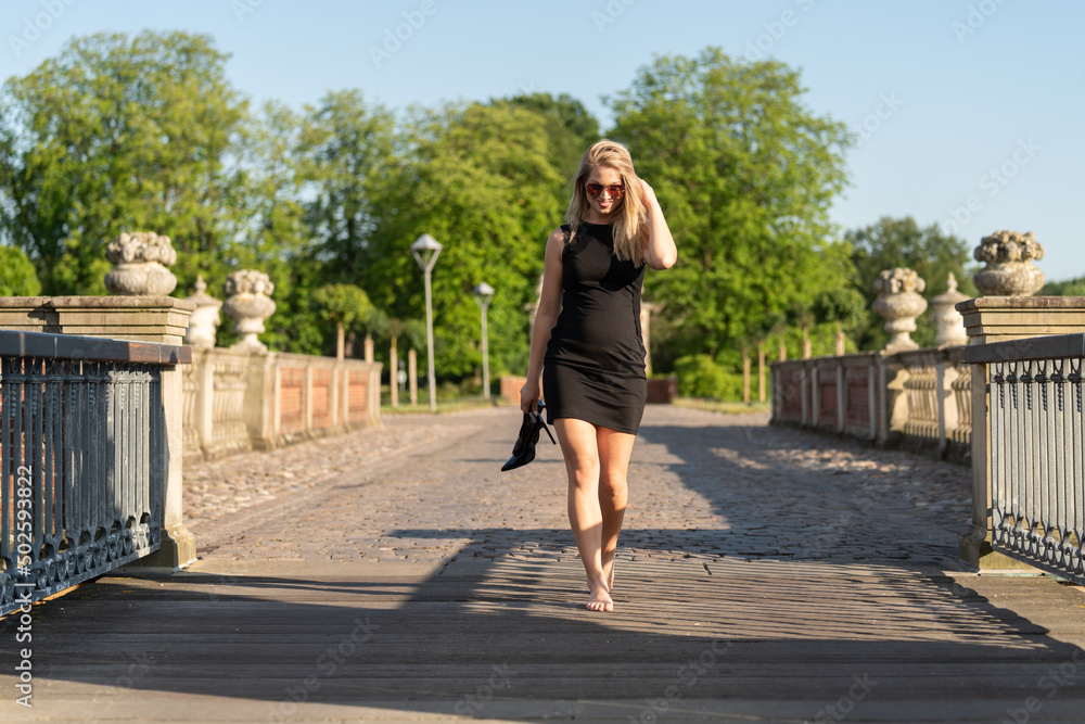 Junge blonde Frau spaziert Barfuß und Pumps im Park