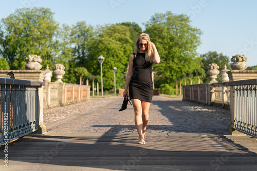 Junge blonde Frau spaziert Barfuß und Pumps im Park