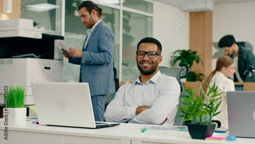 A very handsome young black man is in an aesthetic office as he sits back in his chair crosses his arms and smiles widely