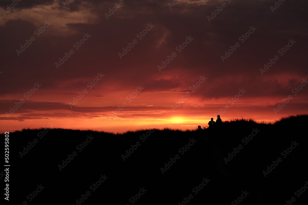 Silhouette of people standing on top of the dunes at sunset. High quality photo
