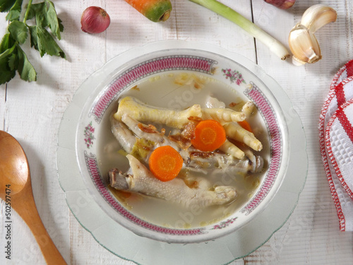 Chicken feet soup, hot and spicy  served in white bowl on wooden table. Known as sop ceker in Indonesia. Commonly mixed with vegetable such as carrot. Delicious, tasty, refreshing. Focus selection. photo