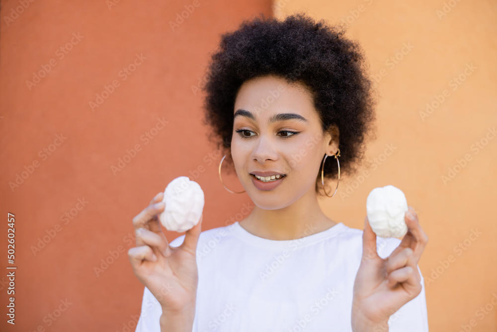 joyful african american woman holding zefir near orange wall