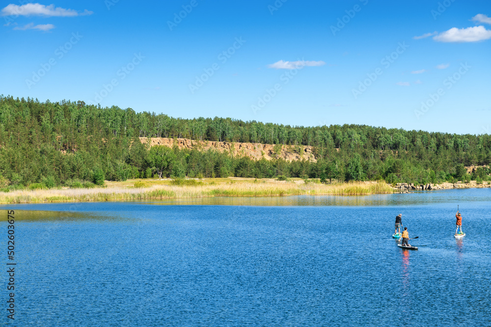 Beautiful scenery of the lake and people doing SUP on nature. Spring and summer landscape
