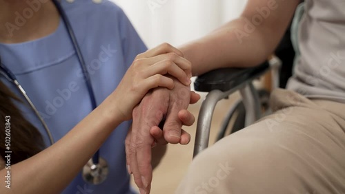 Selective focus with closeup shot hands of medical caregiver tapping hands of older handicapped patient in wheelchair and providing mental support.