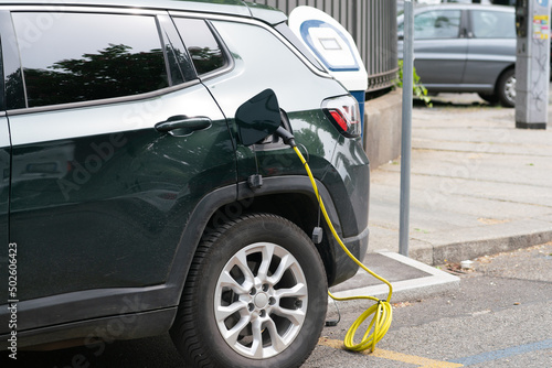 electric vehicle charging, connected with the red cable to the electrical control unit. hybrid car recharges energy zero emissions in cities with green ecological policies. © rikstock