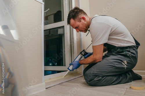 Young man wearing overalls sealing a door photo