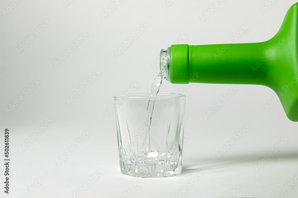 Fototapeta premium Vodka is poured into a glass on a white background. Strong alcoholic drink. Alcohol addiction