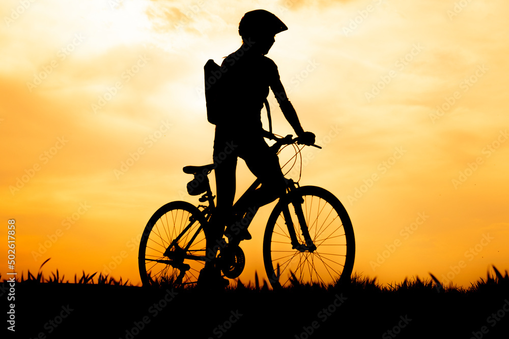Obraz premium Silhouette of cyclist riding a road bike at at sunset with orange sky in countryside.