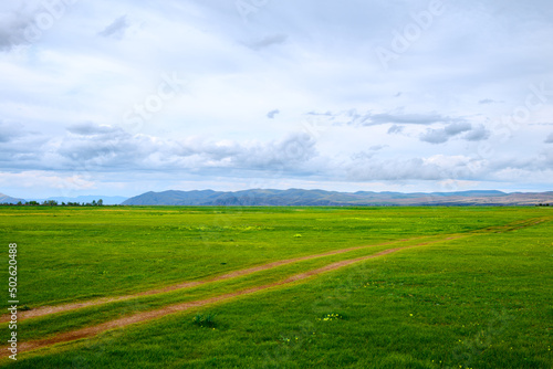 Green hill ranges. Road. Panorama of meadow with green grass, and in the background the sunrise in a small haze.