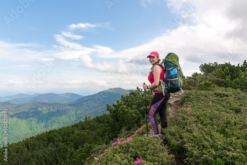 Hiking young woman with backpack and trekking poles on the mountain trail