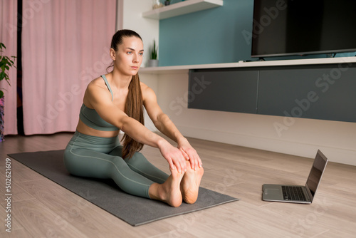 Online Yoga classes. Woman doing virtual yoga from laptop at home for develop core strength, increase flexibility, improve posture, boost energy. Healthy living concept