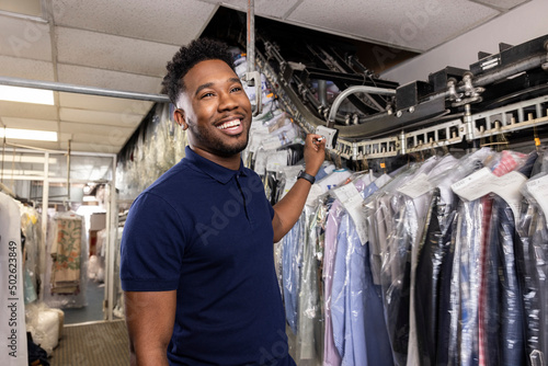Young African American small business owner talking with customer while pulling clothes off rack at dry cleaners