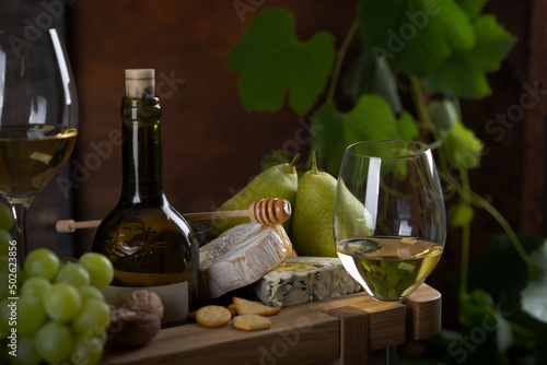White wine in glasses, pear, cheese plate and grapes.