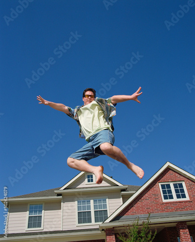 Middle aged man jumping in front of home, striking a pose mid air photo