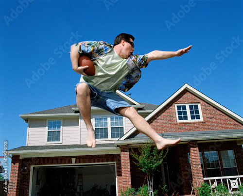 Middle aged man holding a football jumping in front of home, striking a pose mid air photo