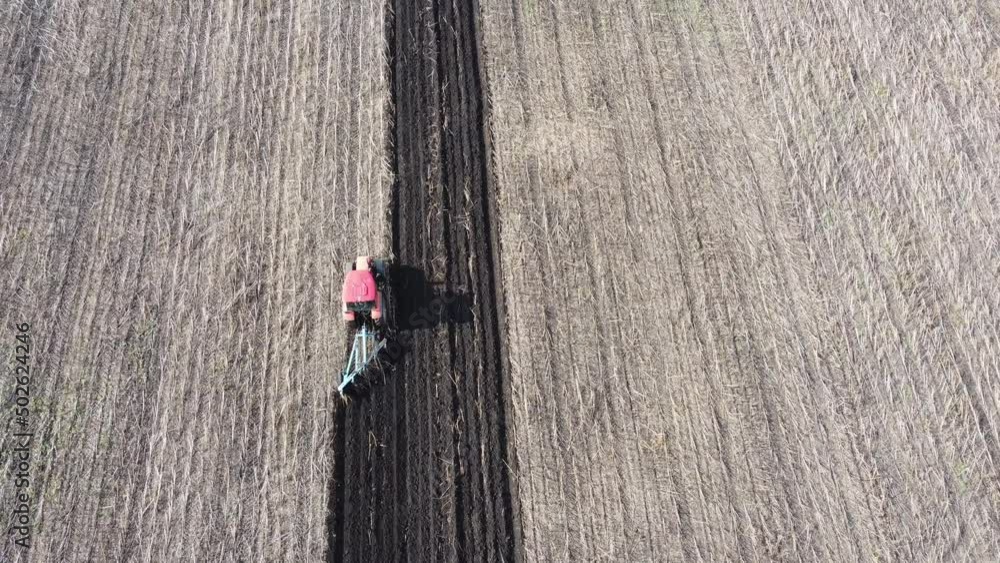 Shooting from drone flying over tractor with harrow system plowing ground on cultivated farm field, pillar of dust trails behind, preparing soil for planting new crop, agriculture concept, top view Shooting from drone flying over tractor with harrow system plowing ground on cultivated farm field, pillar of dust trails behind, preparing soil for planting new crop, agriculture concept, top view