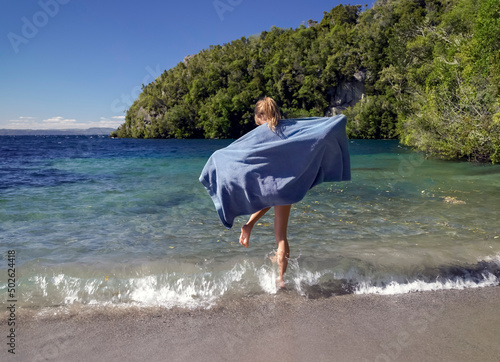 Young woman wearing towel jumping over small waves at lake edge photo