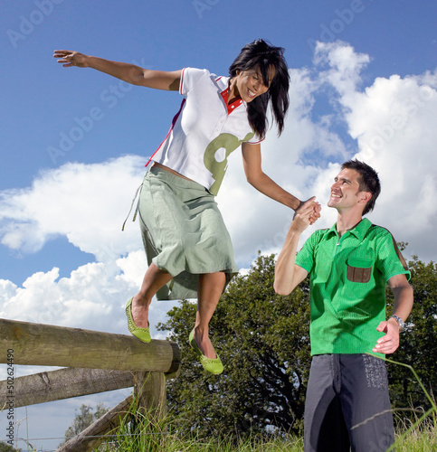 Young man holding young woman's hand as he helps her step down from railing photo