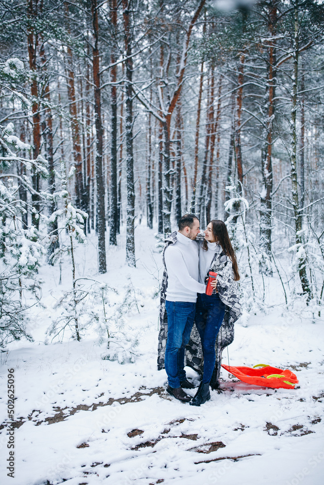 beautiful woman with long hair in a white sweater and a man. winter love story in a snowy forest
