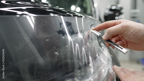 The master cuts the protective film on the car with a knife. Car detailing. Male specialist applying window tinting film on the car and cuts off excess part with a knife. photo