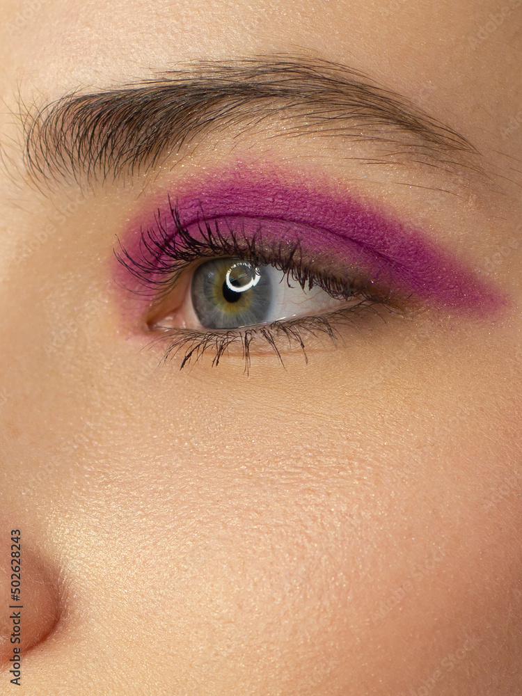 Obraz premium Close eye with colorful eyeshadow. Macro shot of opened human female eye. Woman with evening beauty makeup. Girl with perfect skin and eyebrow. Women cosmetics, extremely long eyelash and pink glitter