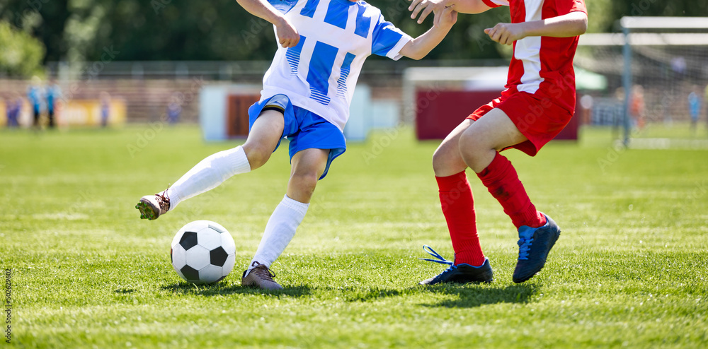 Obraz premium Boys play soccer. Teenagers at school playing soccer in sports field. Children kicking soccer game outdoors. Young male footballers running in red and blue sports uniforms