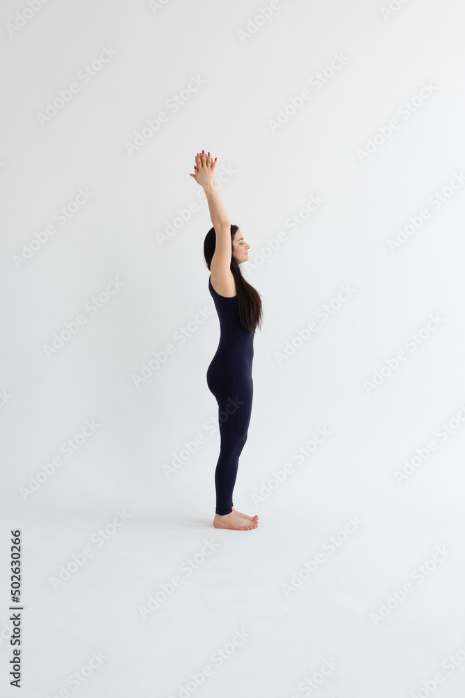 a beautiful young girl with dark hair stands in the Urdhva Hastasana pose on a white background. Yoga class