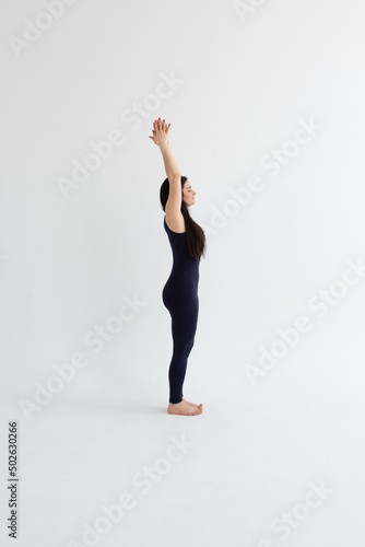 a beautiful young girl with dark hair stands in the Urdhva Hastasana pose on a white background. Yoga class