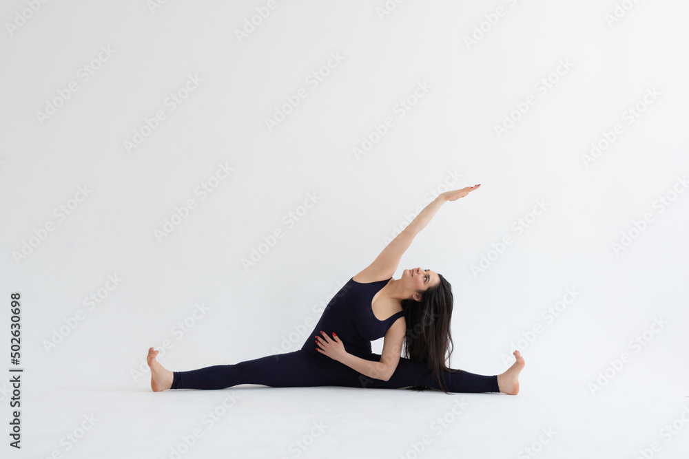 Obraz premium Young beautiful woman practicing yoga on a white background. Young beautiful girl doing exercises at home. Harmony, balance, meditation, relaxation, healthy lifestyle concept 