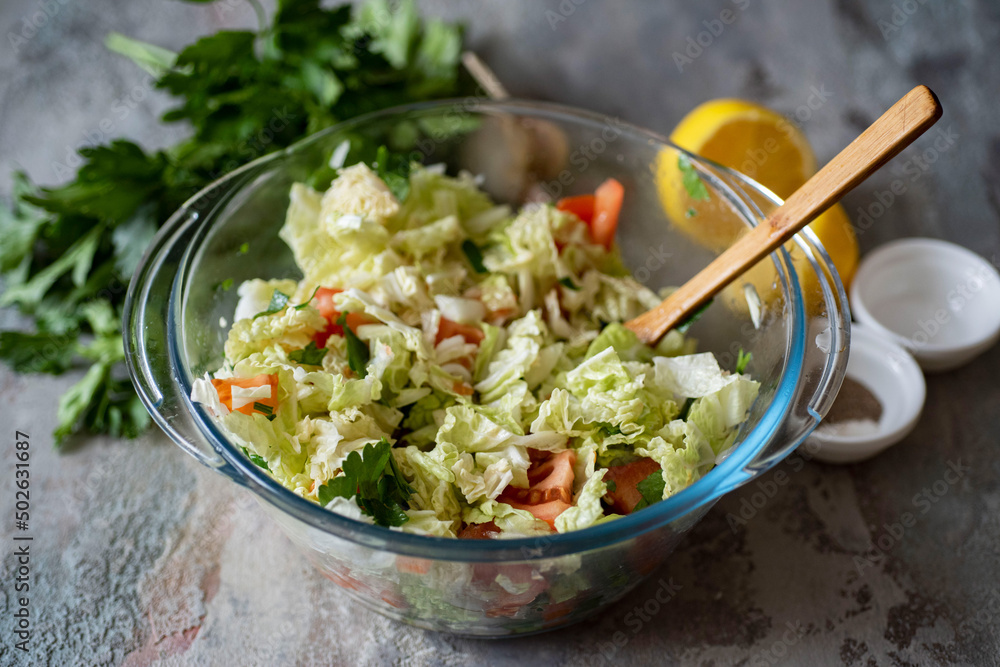 Vegetarian food. Salad of fresh vegetables: cabbage, tomatoes, onions, parsley in a glass bowl on a gray background. Close-up. Vegetarian food. Salad of fresh vegetables: cabbage, tomatoes, onions, parsley in a glass bowl on a gray background. Close-up.