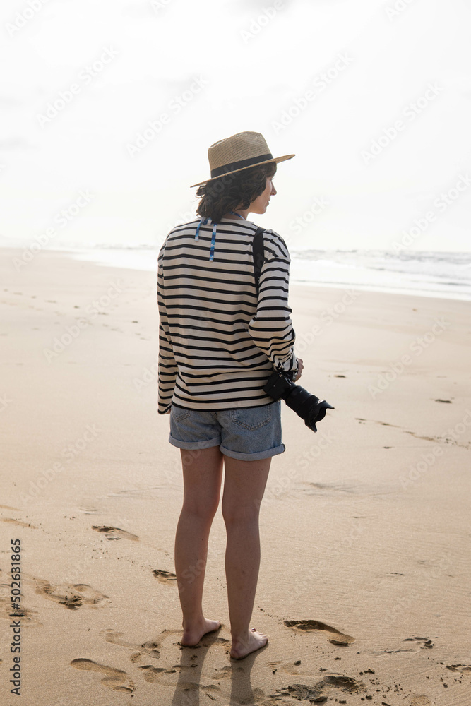 Photo of a young and attractive woman with a photo camera wearing summer clothes at the beach. Photography, holidays, travel.
