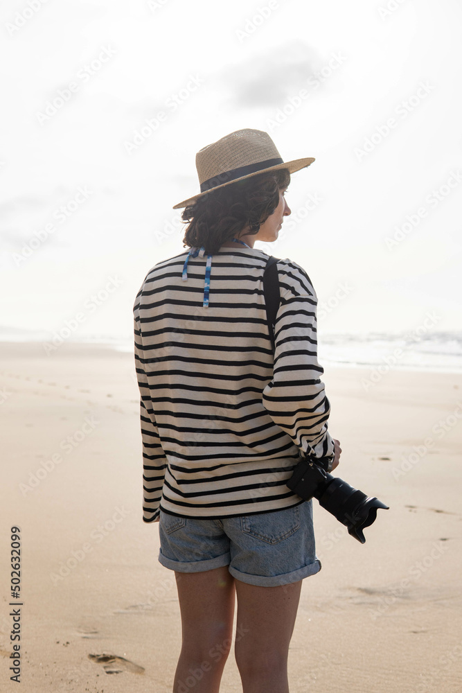 Photo of a young and attractive woman with a photo camera wearing summer clothes at the beach. Photography, holidays, travel.