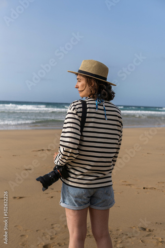 Obraz na płótnie Photo of a young and attractive woman with a photo camera wearing summer clothes at the beach. Photography, holidays, travel. w salonie
