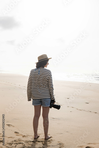 Photo of a young and attractive woman with a photo camera wearing summer clothes at the beach. Photography, holidays, travel. 