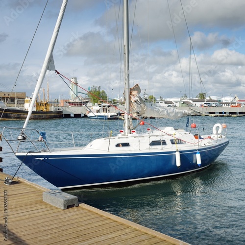 Blue sloop rigged sailboat moored to a pier in a yacht marina. Transportation, sailing, yachting, sport, recreation, leisure activity, cruise, tourism, lifestyle, service and repair themes
