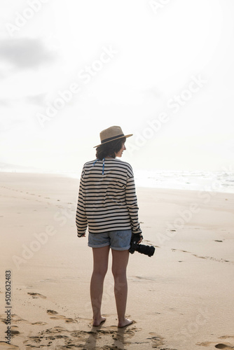 Photo of a young and attractive woman with a photo camera wearing summer clothes at the beach. Photography, holidays, travel. 