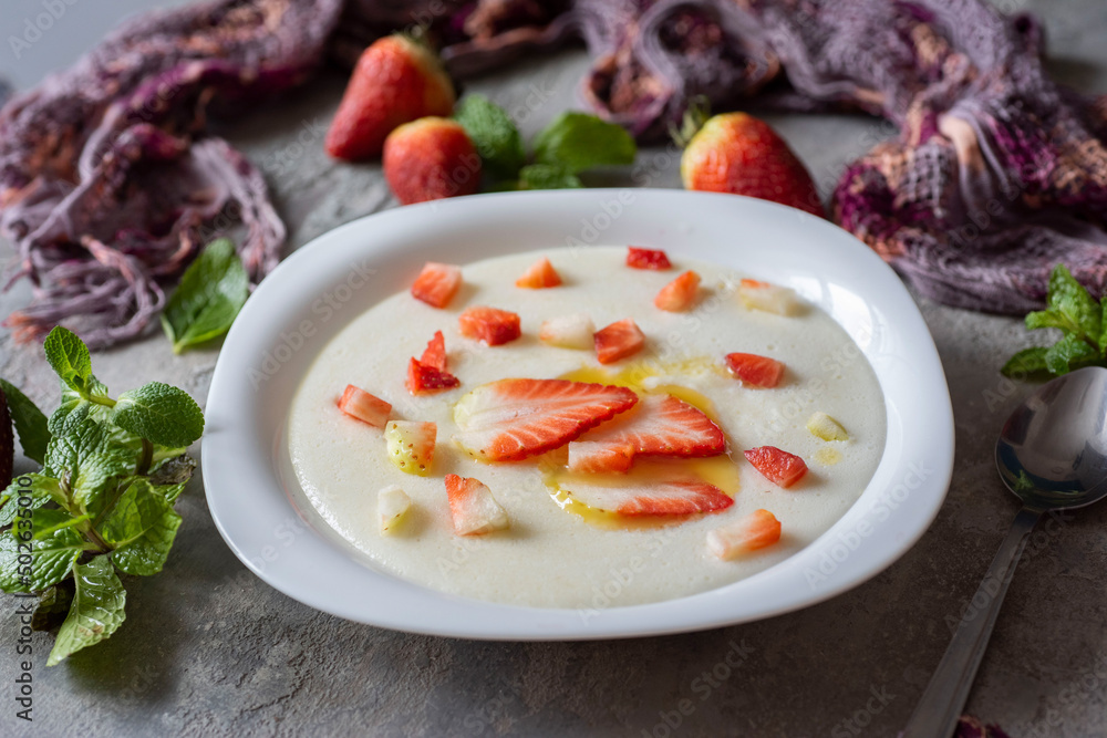 Breakfast for the whole family: semolina porridge with milk with strawberry slices and butter in a beautiful plate on a gray background. Porridge for children. Close-up. Breakfast for the whole family: semolina porridge with milk with strawberry slices and butter in a beautiful plate on a gray background. Porridge for children. Close-up.