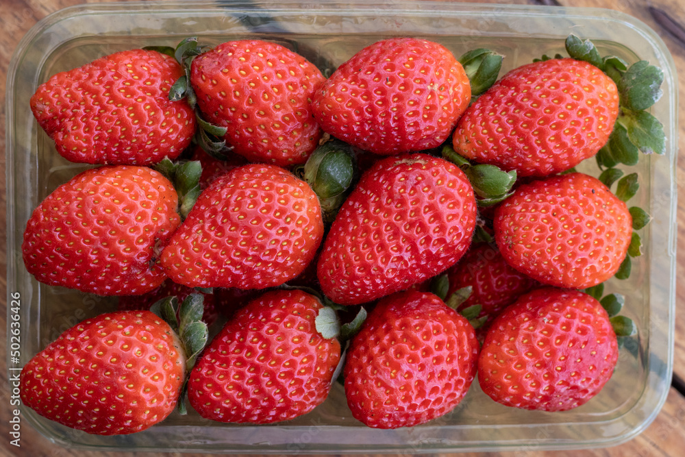 Red ripe strawberries in clear plastic tray, on wooden table