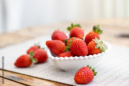 Delicious ripe fresh strawberries in a white bowl on a wooden table background