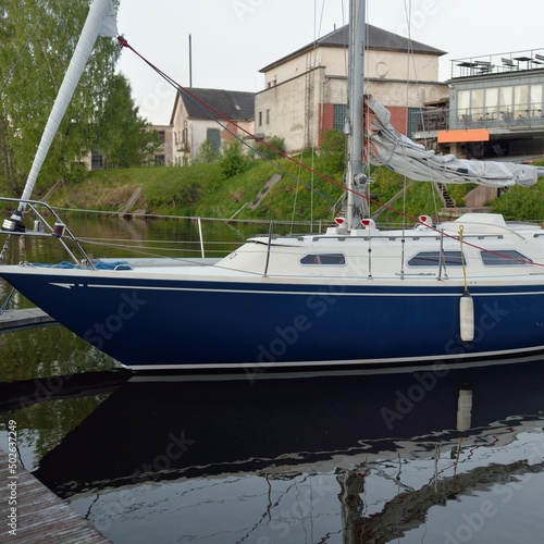 Blue sloop rigged sailboat moored to a pier in a yacht marina. Transportation, sailing, yachting, sport, recreation, leisure activity, cruise, tourism, lifestyle, service and repair themes