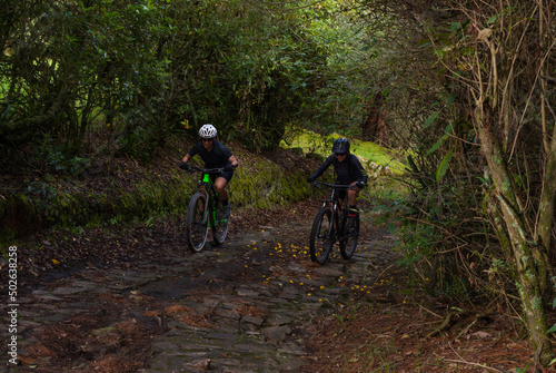 Two women cyclists climbing a trail in the middle of nature