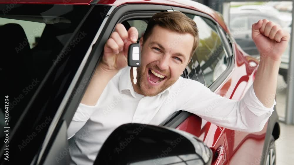 The man with keys shows emotions of happiness while driving in her new car. The buyer selects a car The man with keys shows emotions of happiness while driving in her new car. The buyer selects a car
