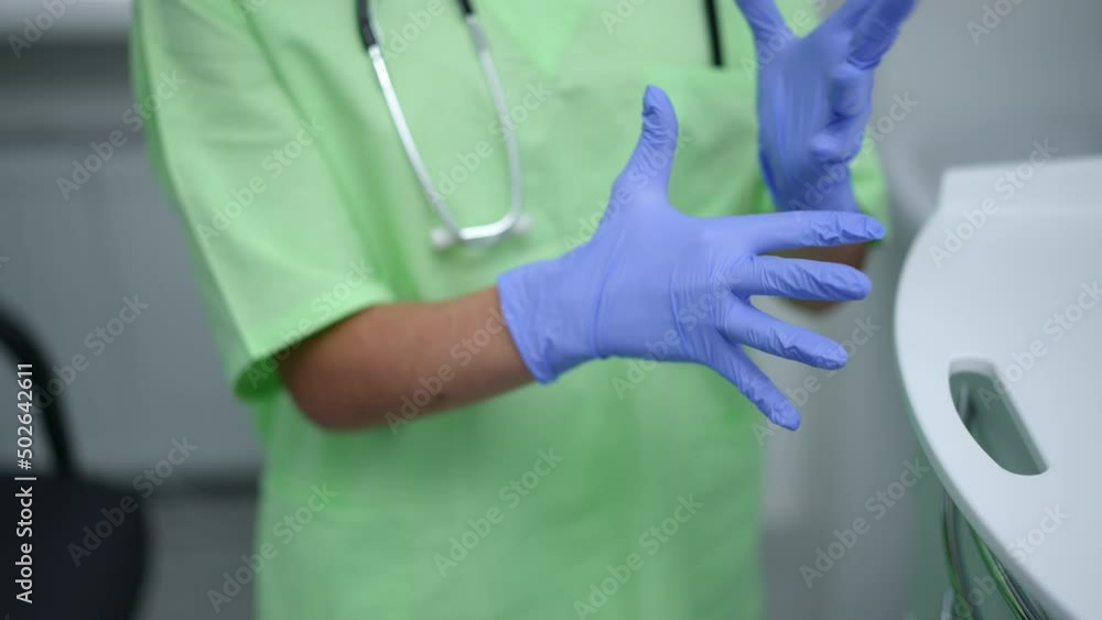 Unrecognizable woman putting on medical gloves standing in hospital indoors. Young slim Caucasian doctor preparing for examination in clinic. Health care and expertise concept Unrecognizable woman putting on medical gloves standing in hospital indoors. Young slim Caucasian doctor preparing for examination in clinic. Health care and expertise concept