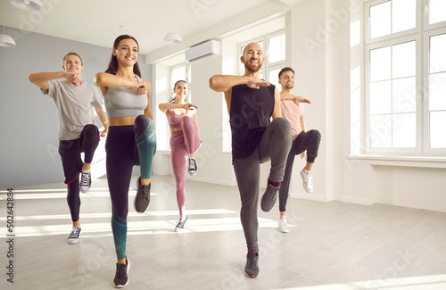 Smiling people in sportswear do sports exercise in bright studio. Happy young dancers crew or team train dance together. Hobby and entertainment concept. Physical activity and workout.